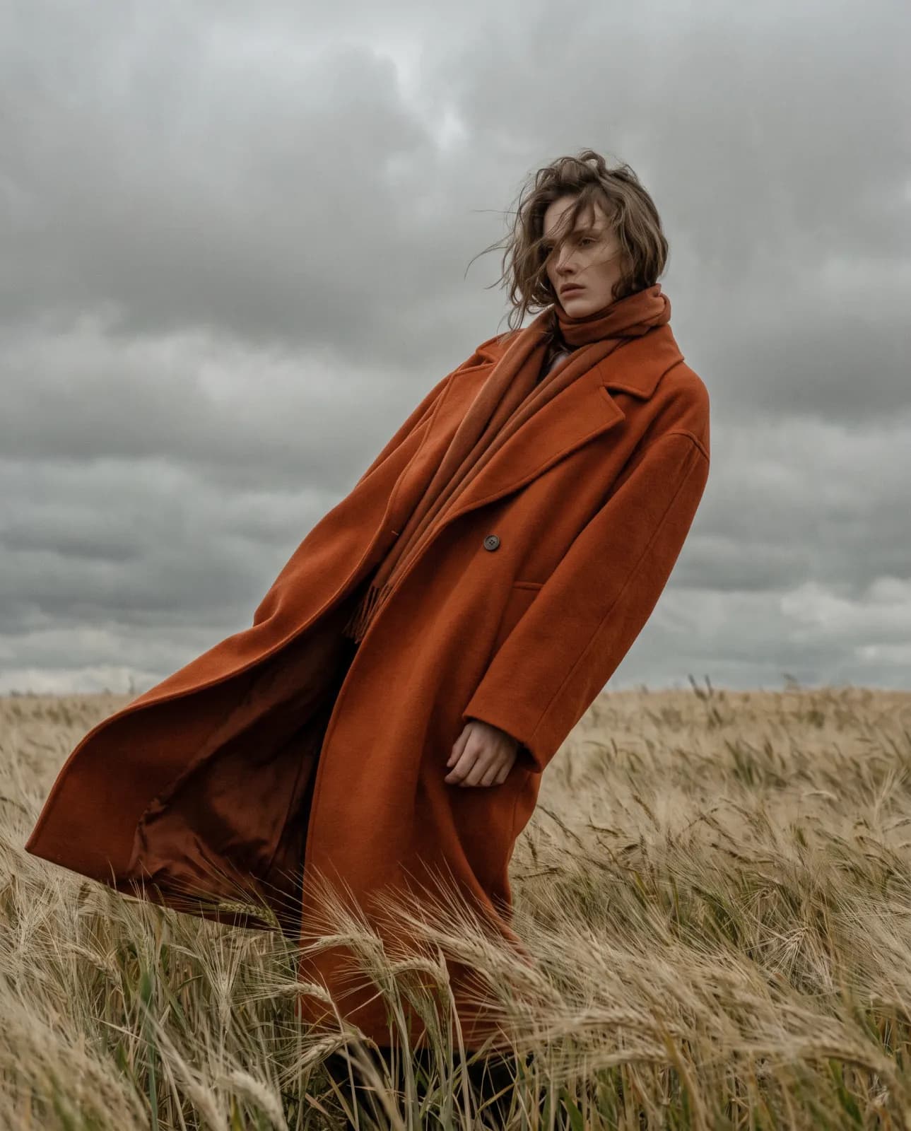 Model in an orange coat walking through a wheat field